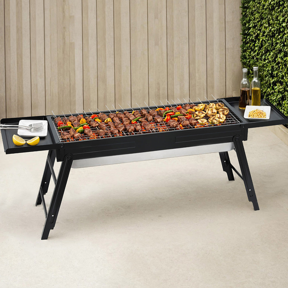 Portable charcoal BBQ grill with foldable legs, side shelves, open cooking grate.