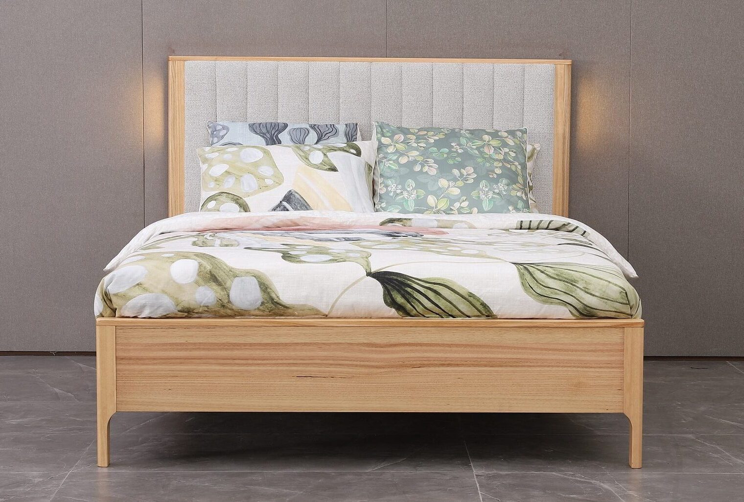 Wooden bed with floral bedding and patterned headboard against a gray wall.