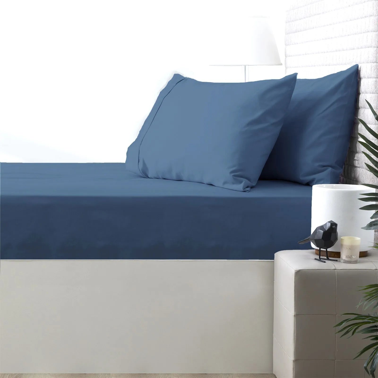 Blue bed sheets and pillows on a bed with a nightstand in the background.