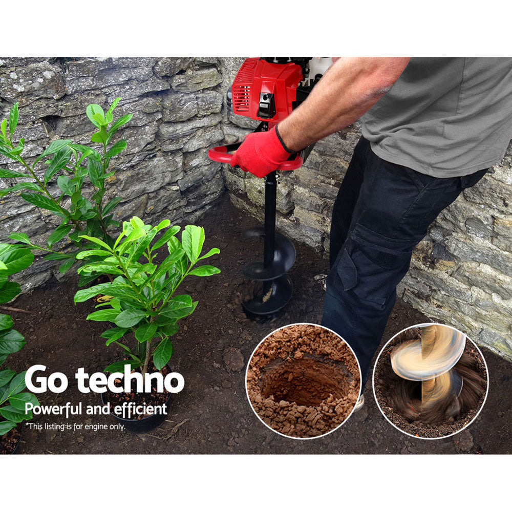 Red petrol post hole digger engine in use with soil auger beside a stone wall
