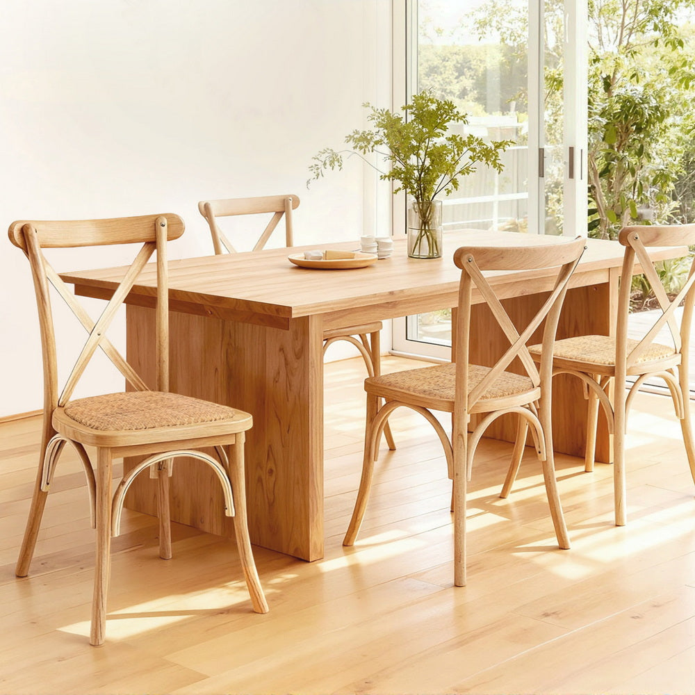 Wooden dining chairs with cross-back frames and woven rattan seats around a table