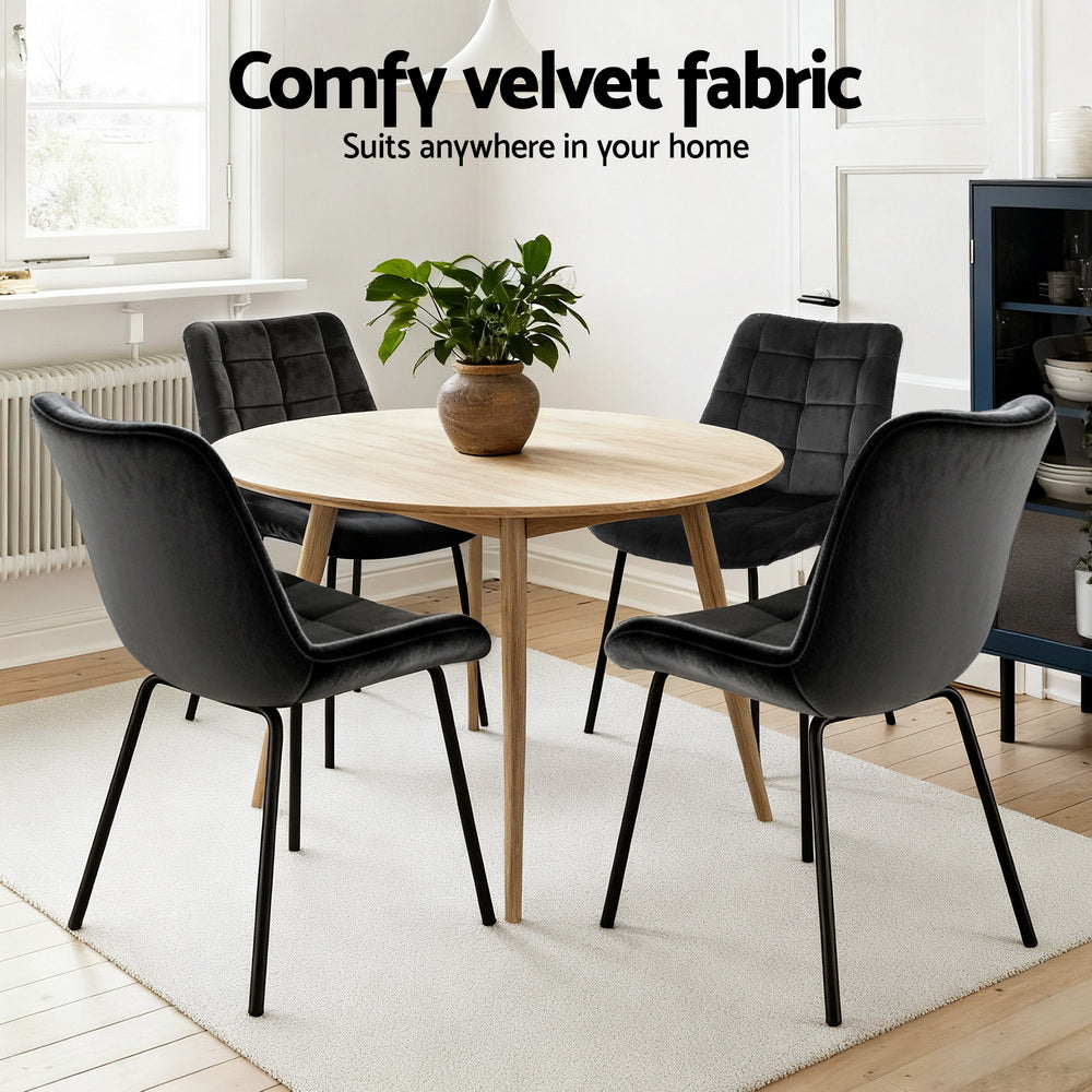 Set of black velvet tufted dining chairs with curved armrests and cushioned seats, metal legs