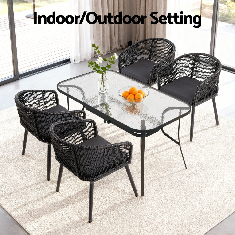 Outdoor dining set with glass table and four woven chairs for patio or indoor use