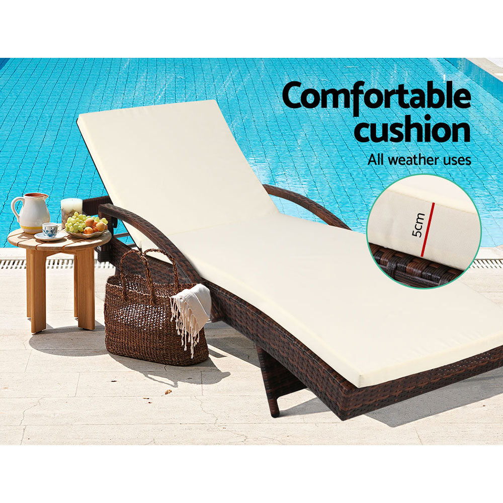 Brown wicker lounge chair with thick cream cushion and arched armrest supports