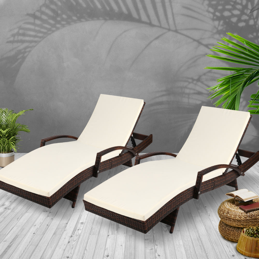Pair of dark brown wicker chaise loungers with cream cushions and curved armrests