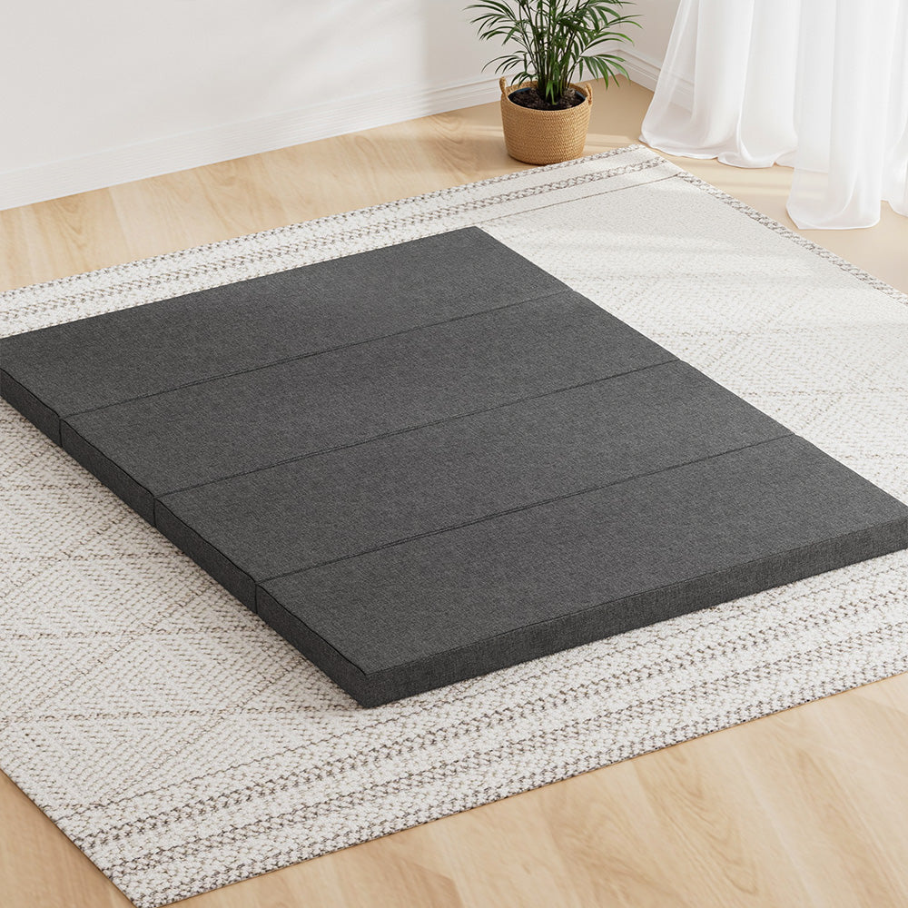 Dark gray foldable foam mattress lying on a woven rug