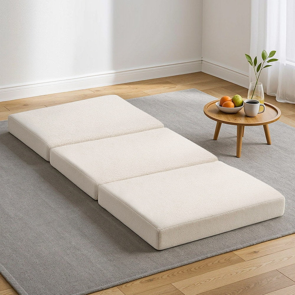 3-fold portable foam mattress in light beige, fully unfolded on the floor.