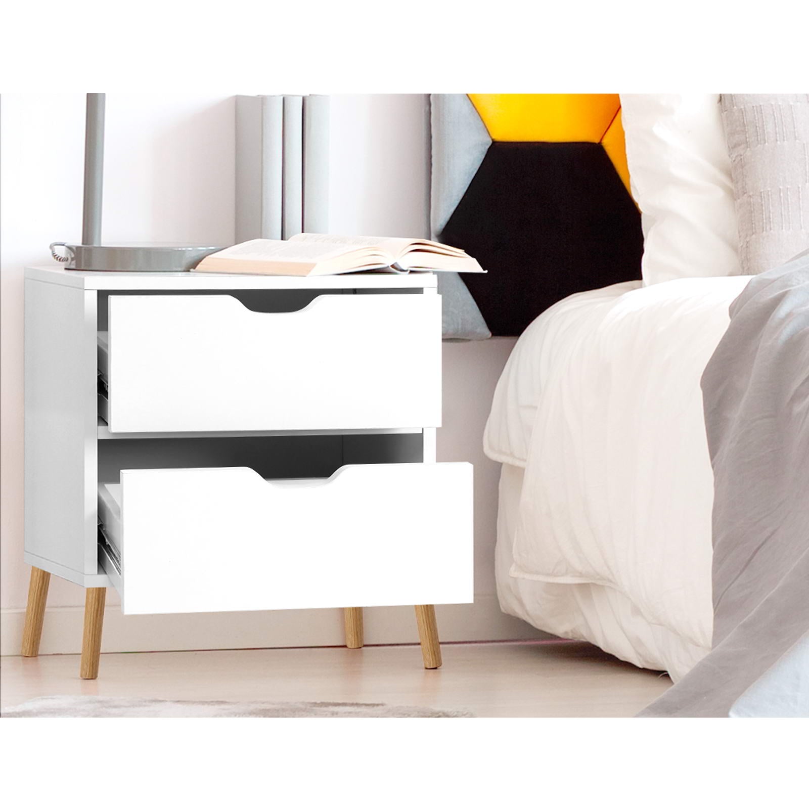 White bedside table with two drawers and black handle cutouts on wooden legs