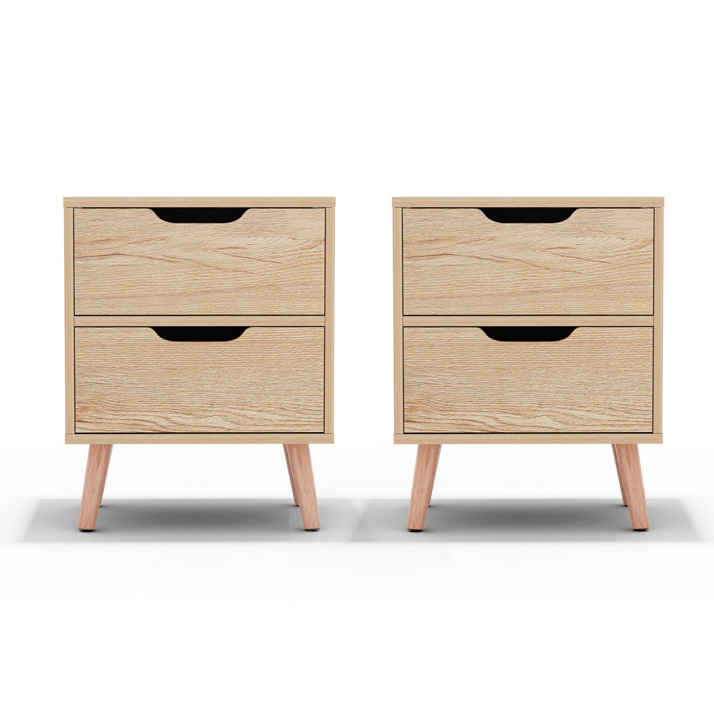 Pair of light pine bedside tables with two drawers each, featuring black handle cutouts and tapered legs.