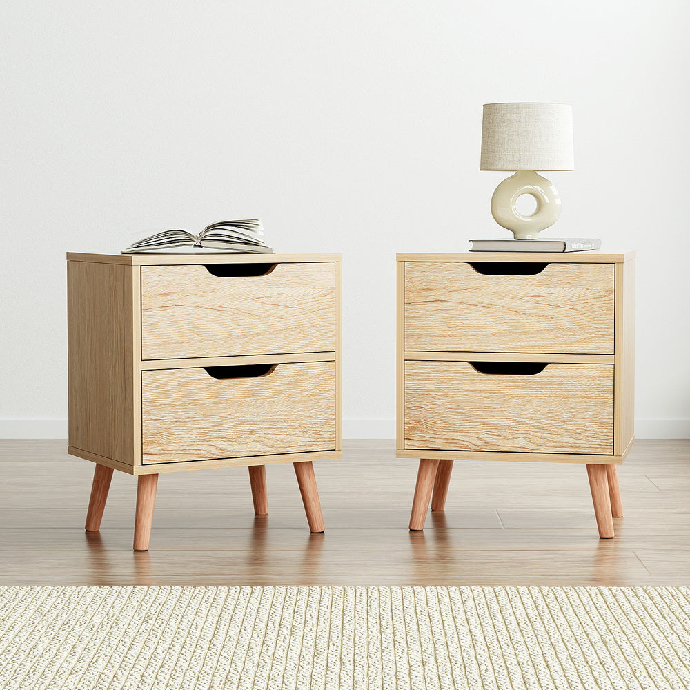 Pair of light pine bedside tables with two drawers, black handle cutouts, and tapered wooden legs.