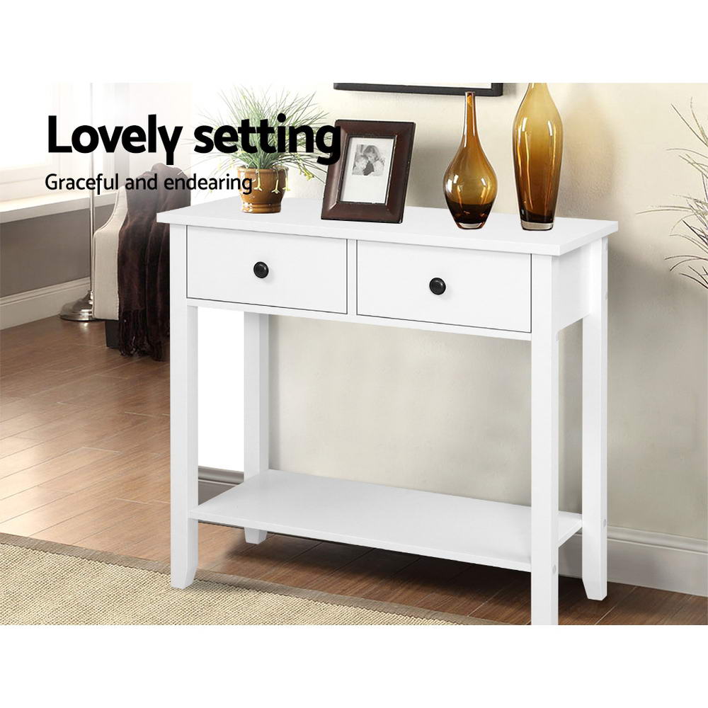 White console table with two drawers and lower shelf, styled with framed photo and vases