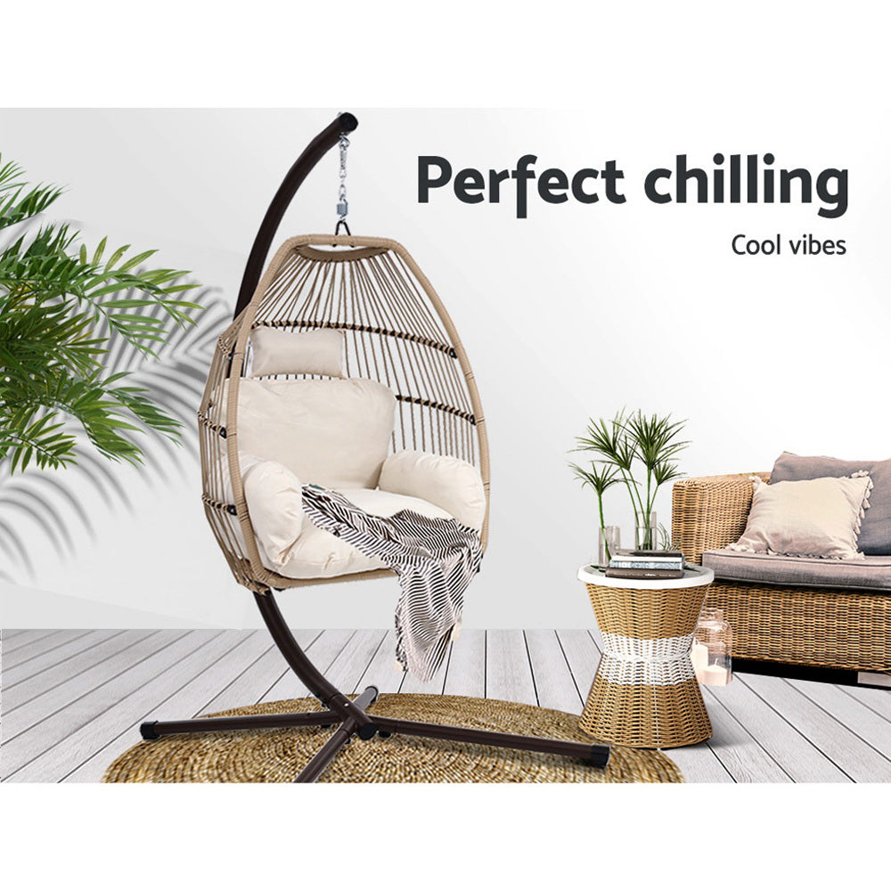 Wicker egg swing chair with beige cushion and dark curved stand base, outdoor view