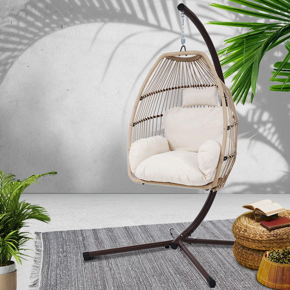 Wicker egg swing chair with beige cushion and dark curved frame on tripod base