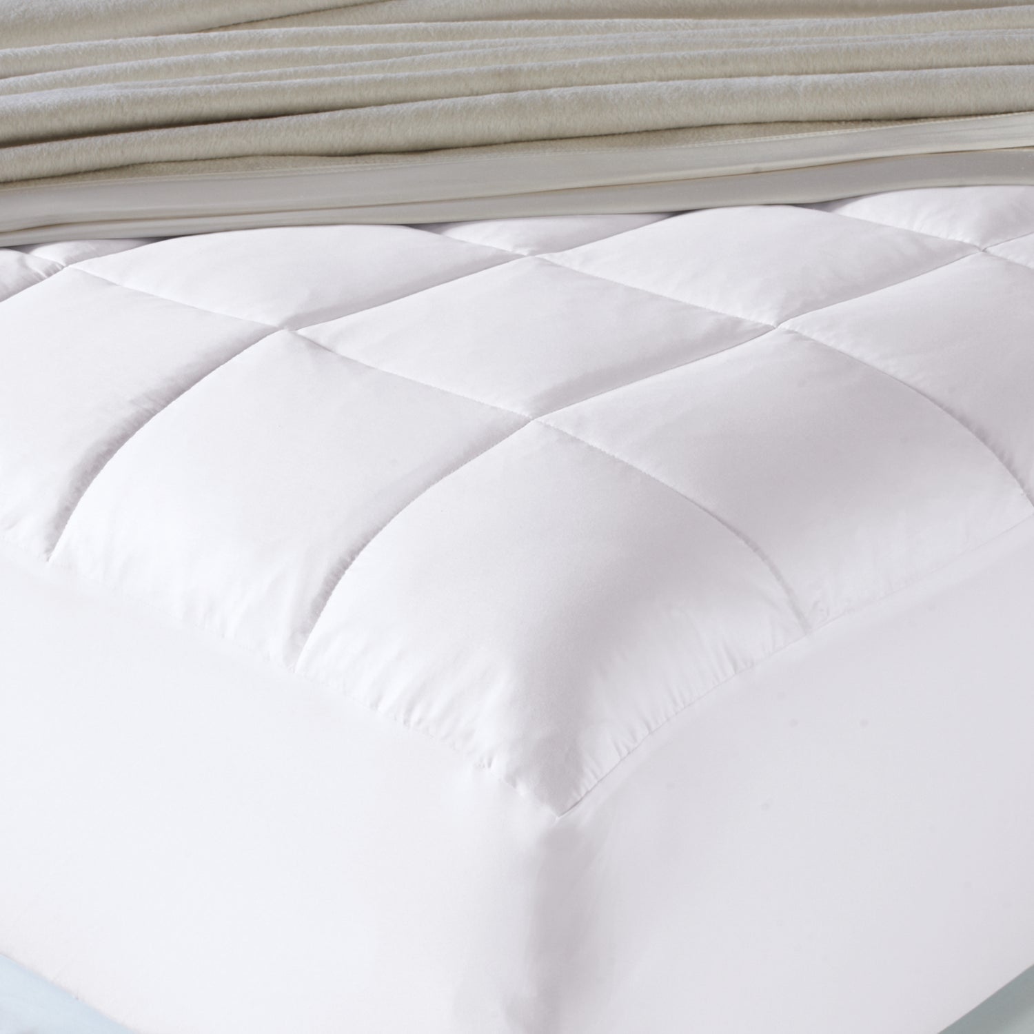 Close-up of a white quilted mattress pad with folded beige blanket in the background.