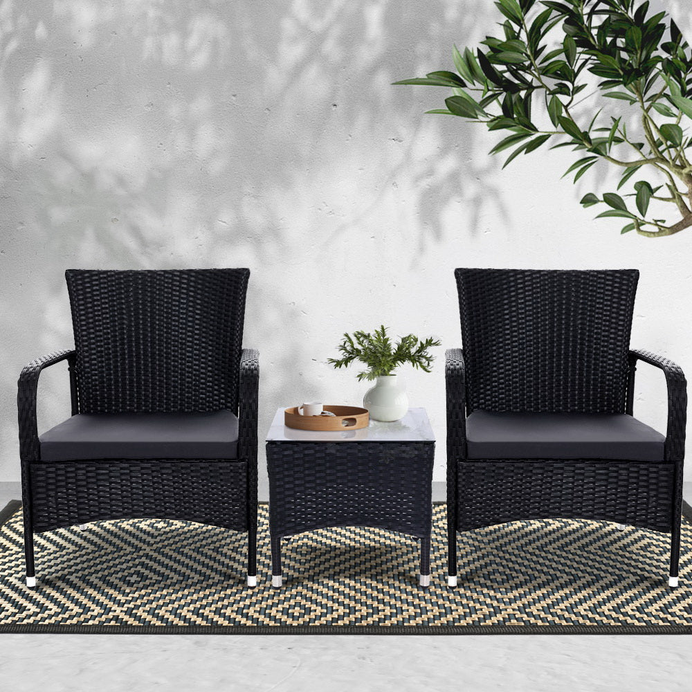 Outdoor bistro set with two black wicker armchairs and a small side table with decor