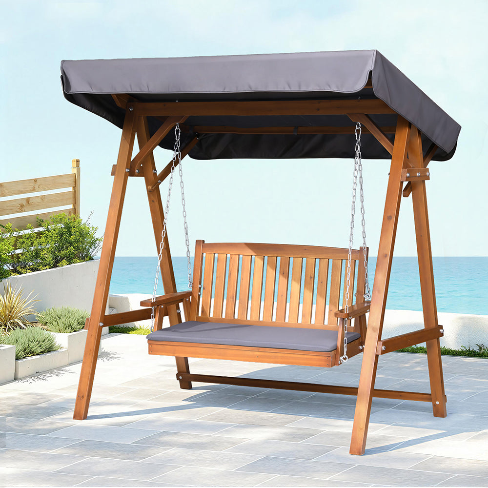 Outdoor wooden swing bench with canopy and dark gray seat cushion, hanging on chains
