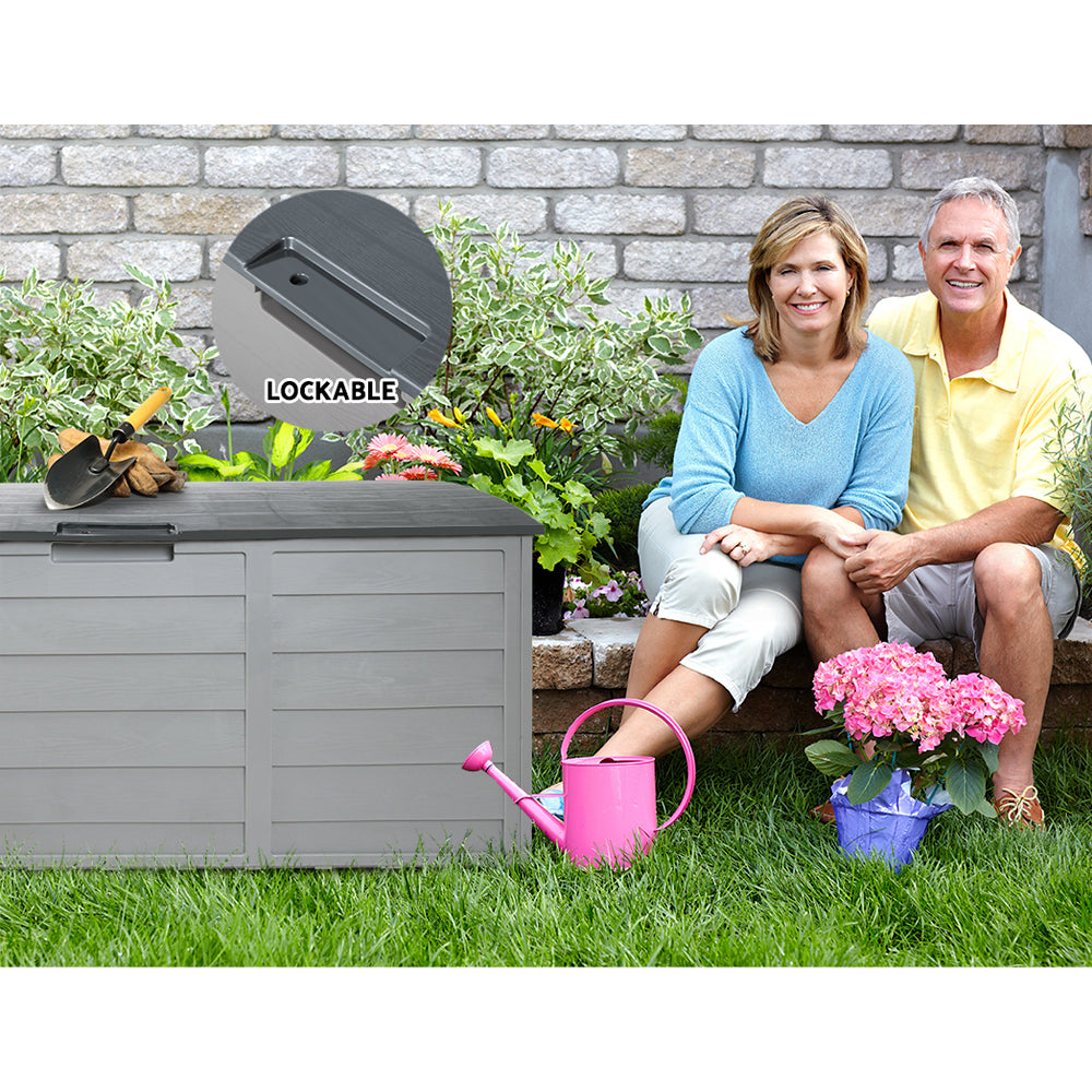 Lockable outdoor storage box with dark lid and lock detail in a garden setting.