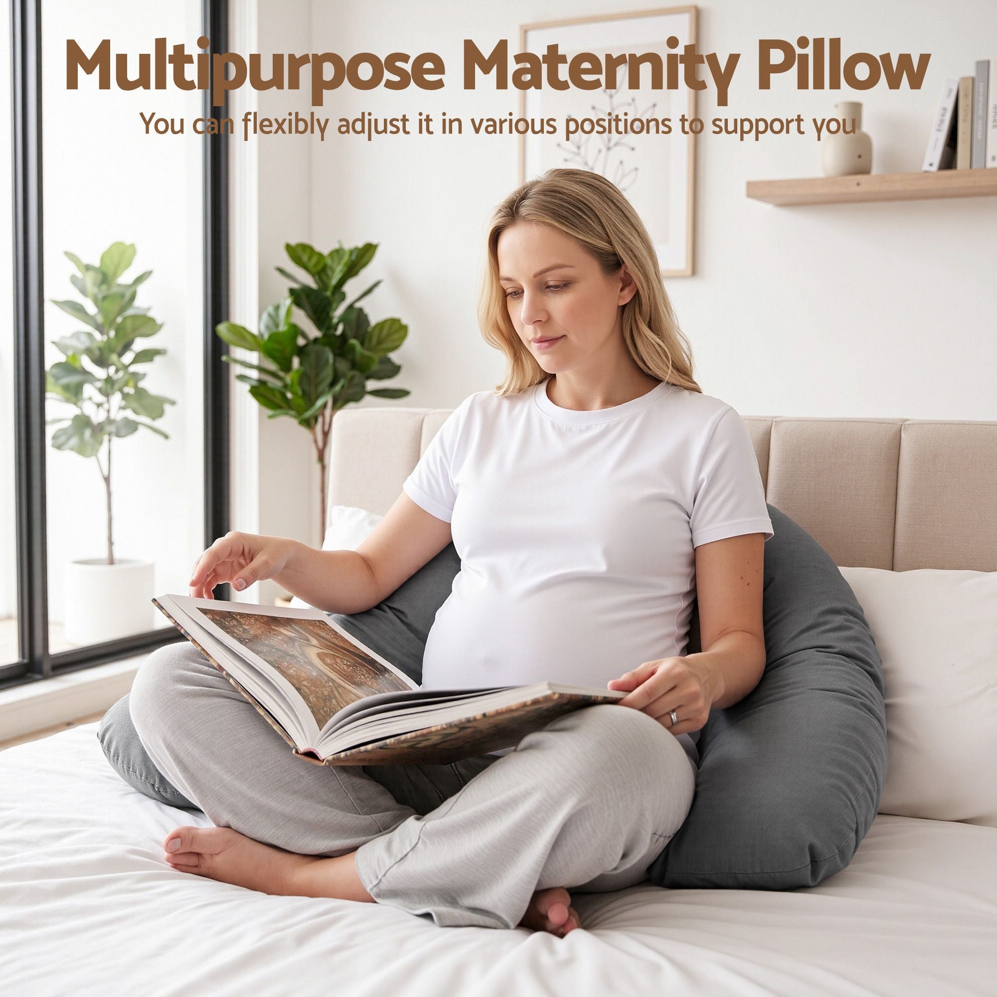 Grey maternity pillow next to a woman sitting on a bed, curved support shape.