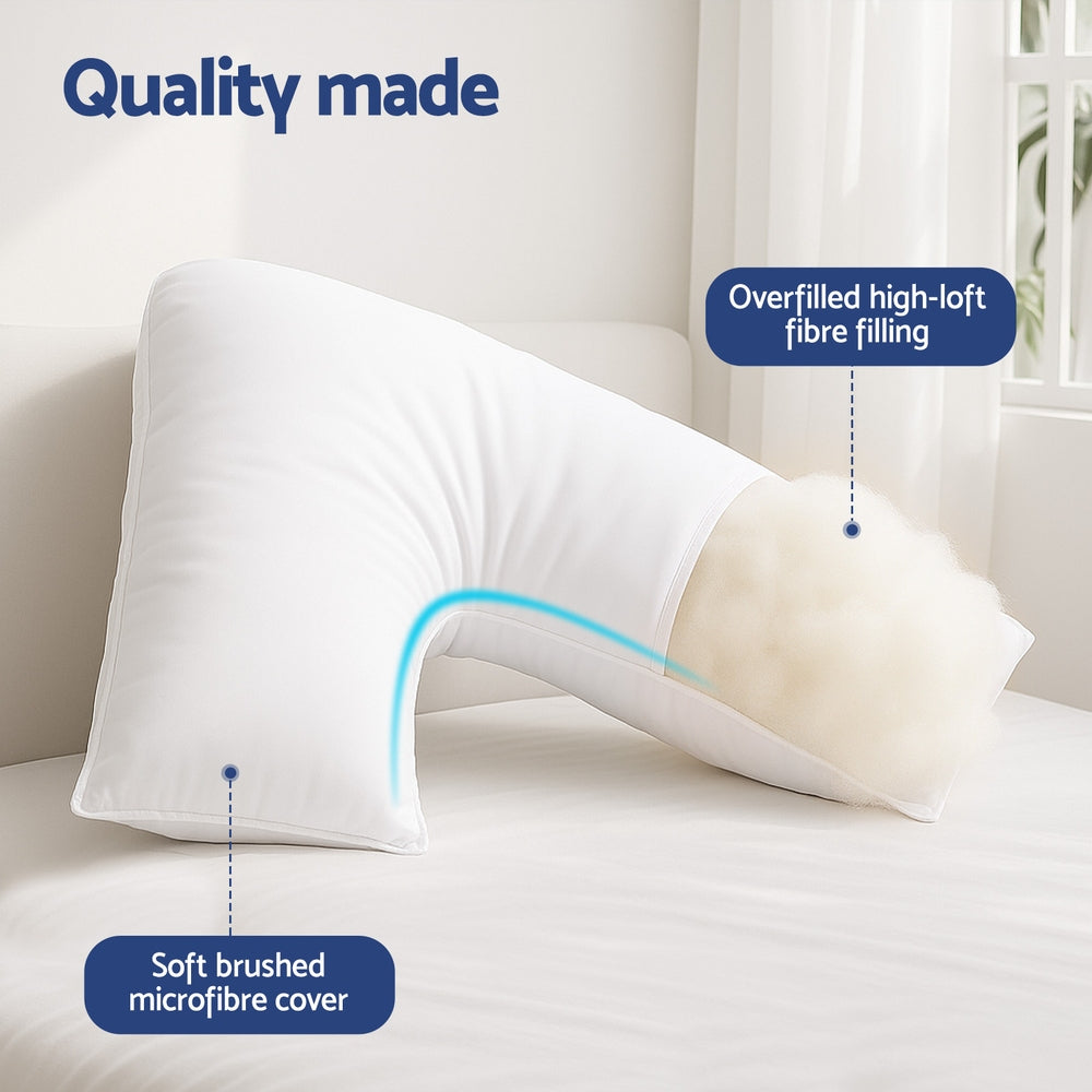 White V-shaped nursing body cushion on a bed, supporting side and back comfort.