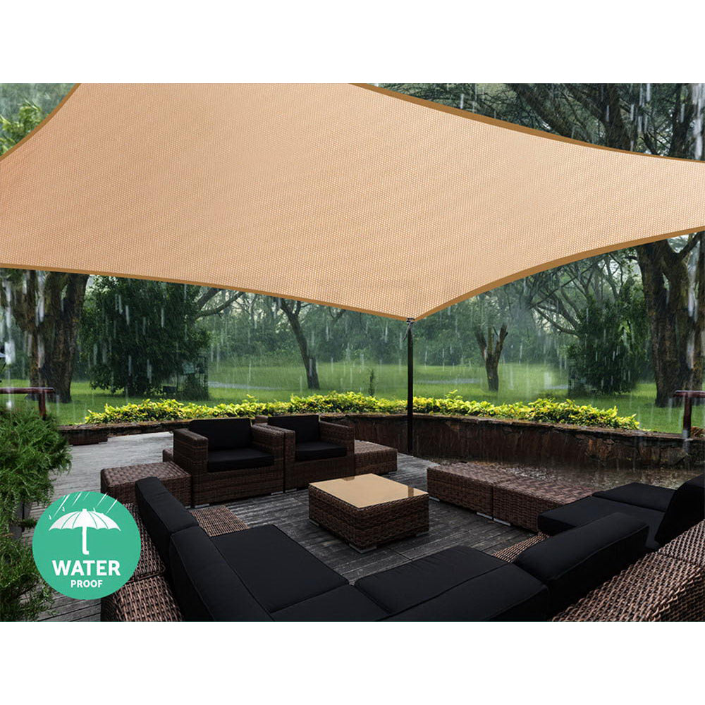 Sand rectangle shade sail overhead over outdoor lounge furniture in yard setting.