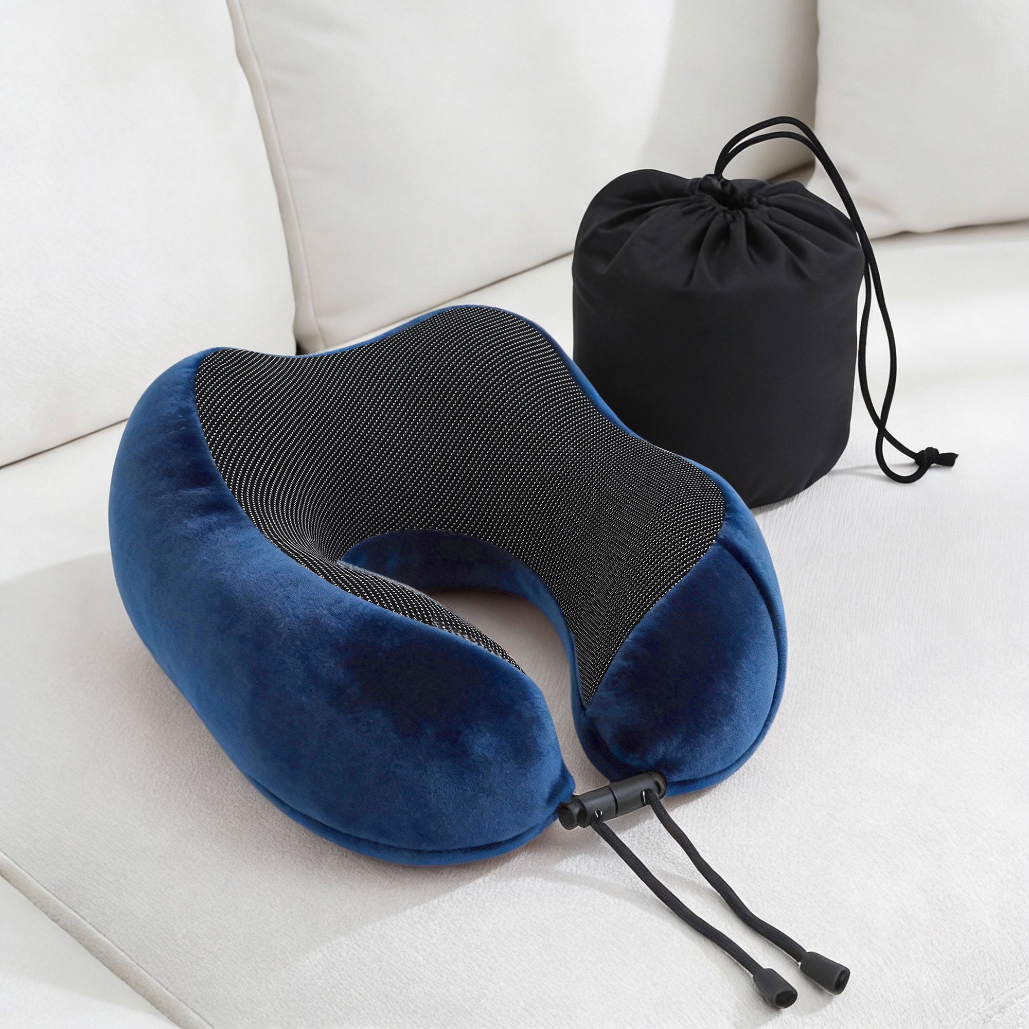 Blue travel neck pillow on a sofa with black tie straps and a matching storage bag