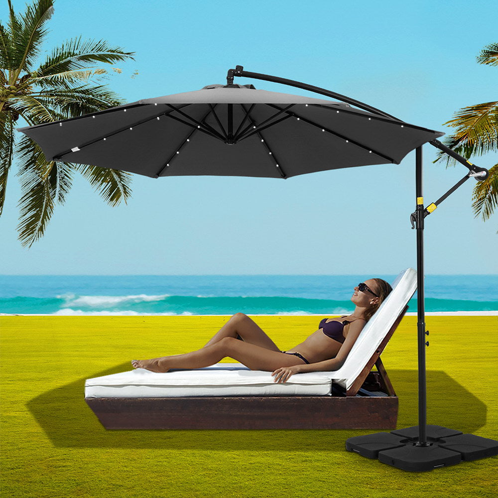 Charcoal cantilever patio umbrella beside weighted base with open black canopy