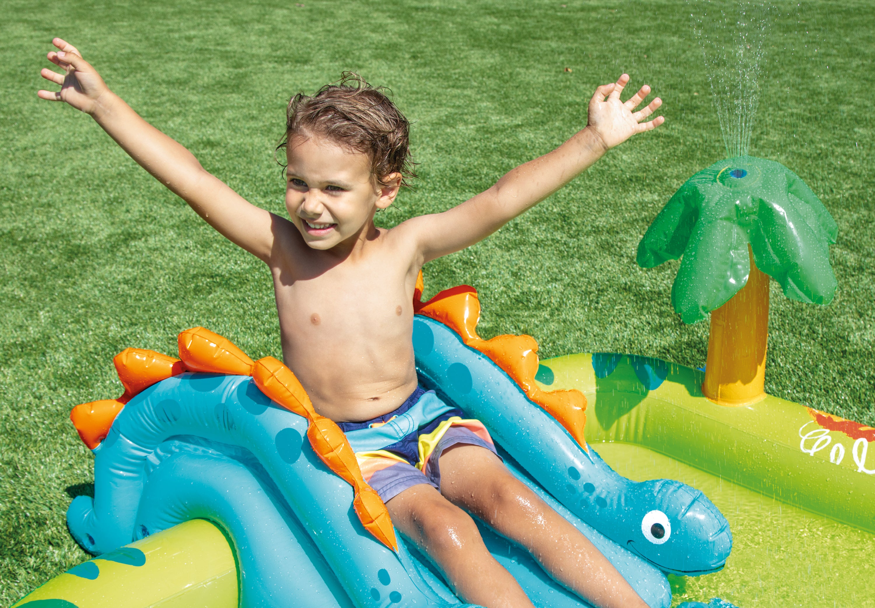 Dinosaur inflatable play centre with blue slide, green pool and child sitting inside