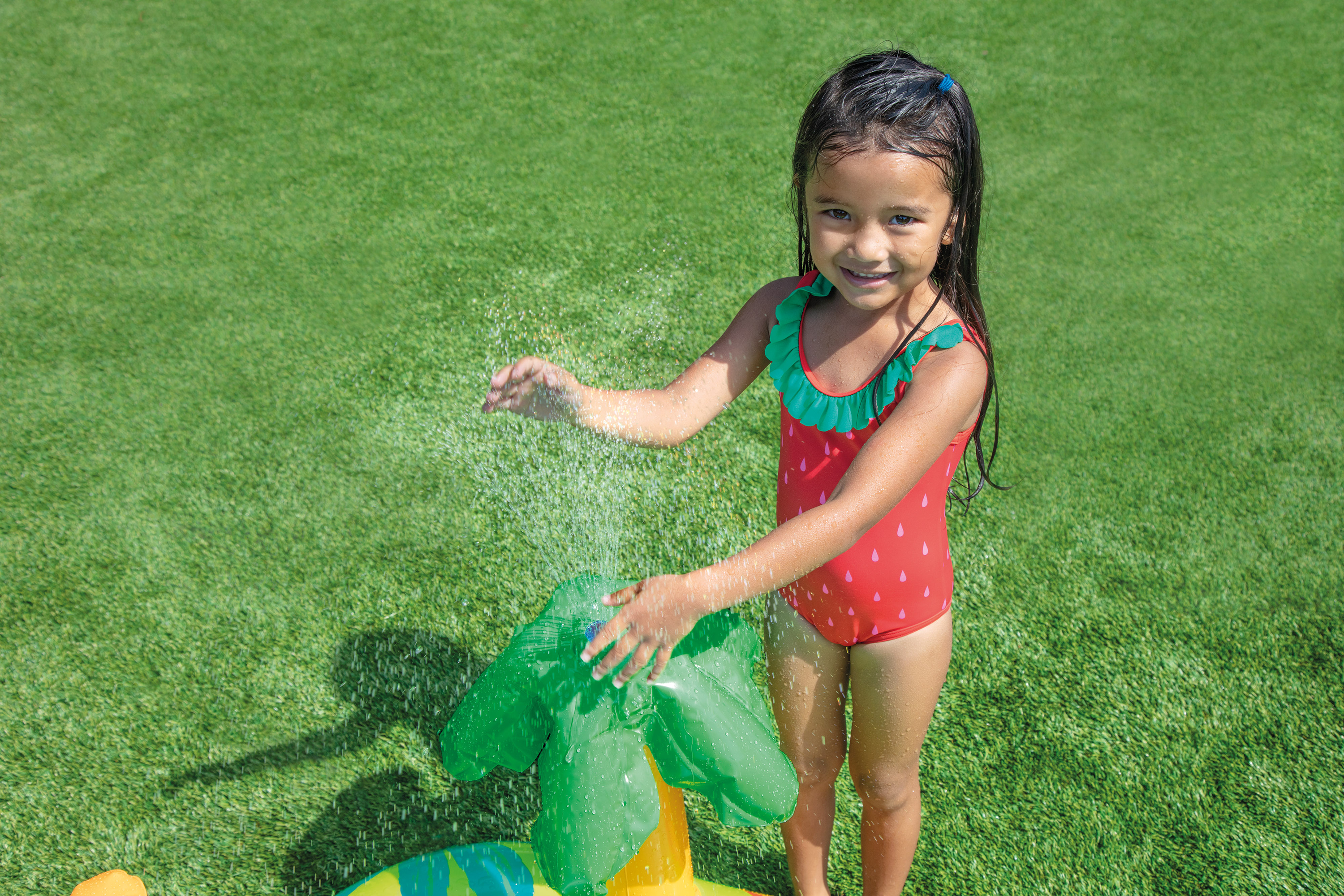 Child next to dinosaur inflatable play centre, showing green pool and orange dinosaur