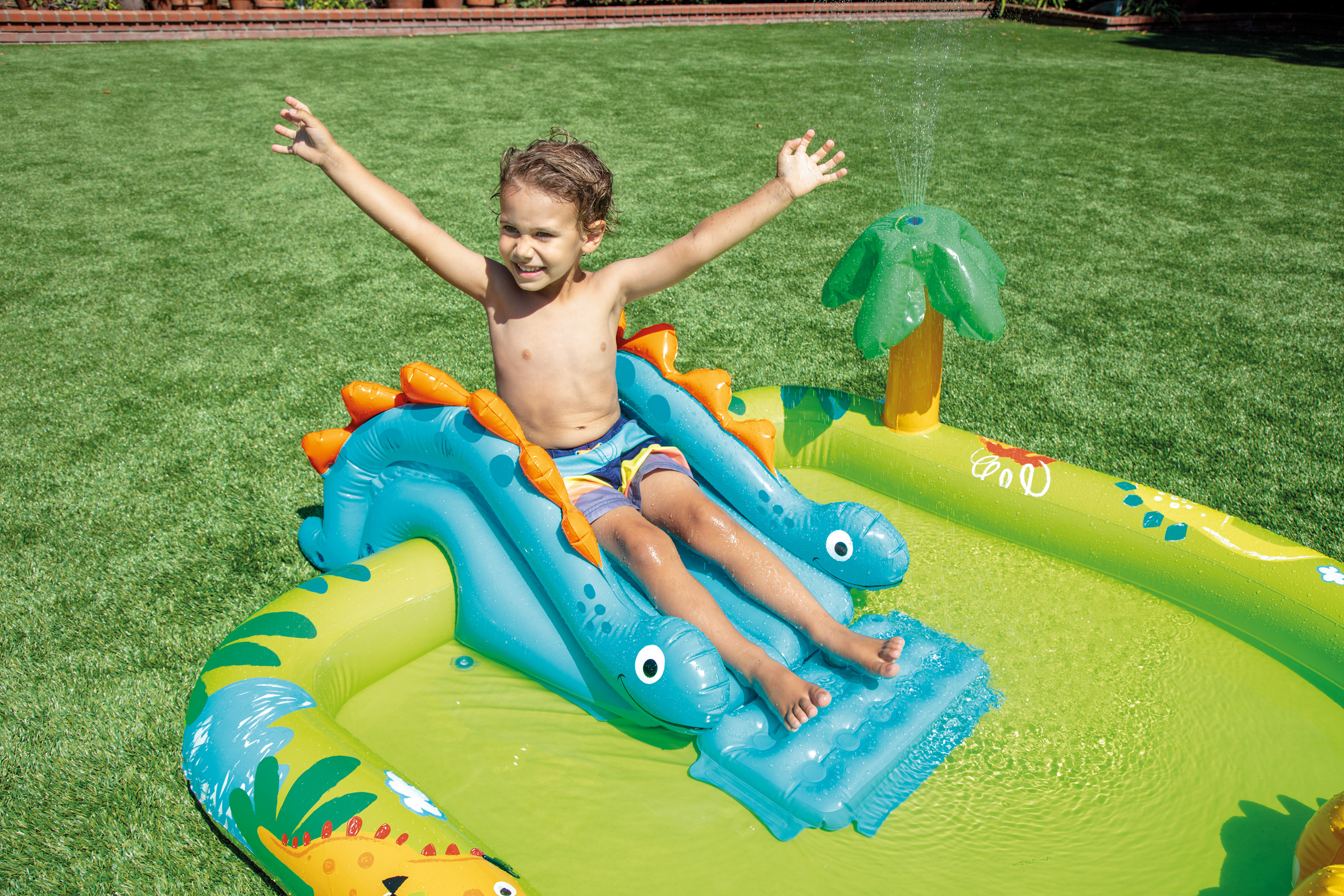 Dinosaur inflatable play centre with blue slide and tree canopy, child sitting