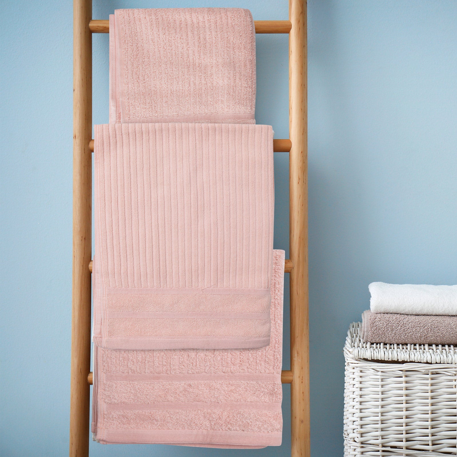 Blush bath towels set folded on a wooden ladder, showing multiple sizes.
