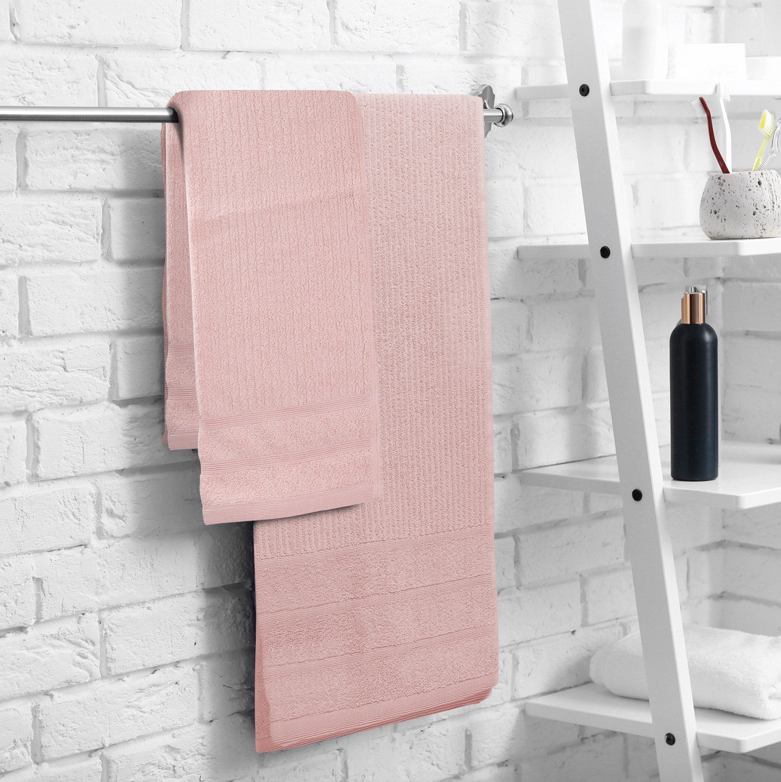 Blush bath towel set hanging on a rail, layered with matching folded towels.