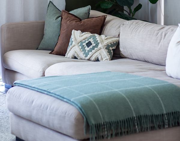 Sage green wool throw blanket with white stripes and fringed hem on couch