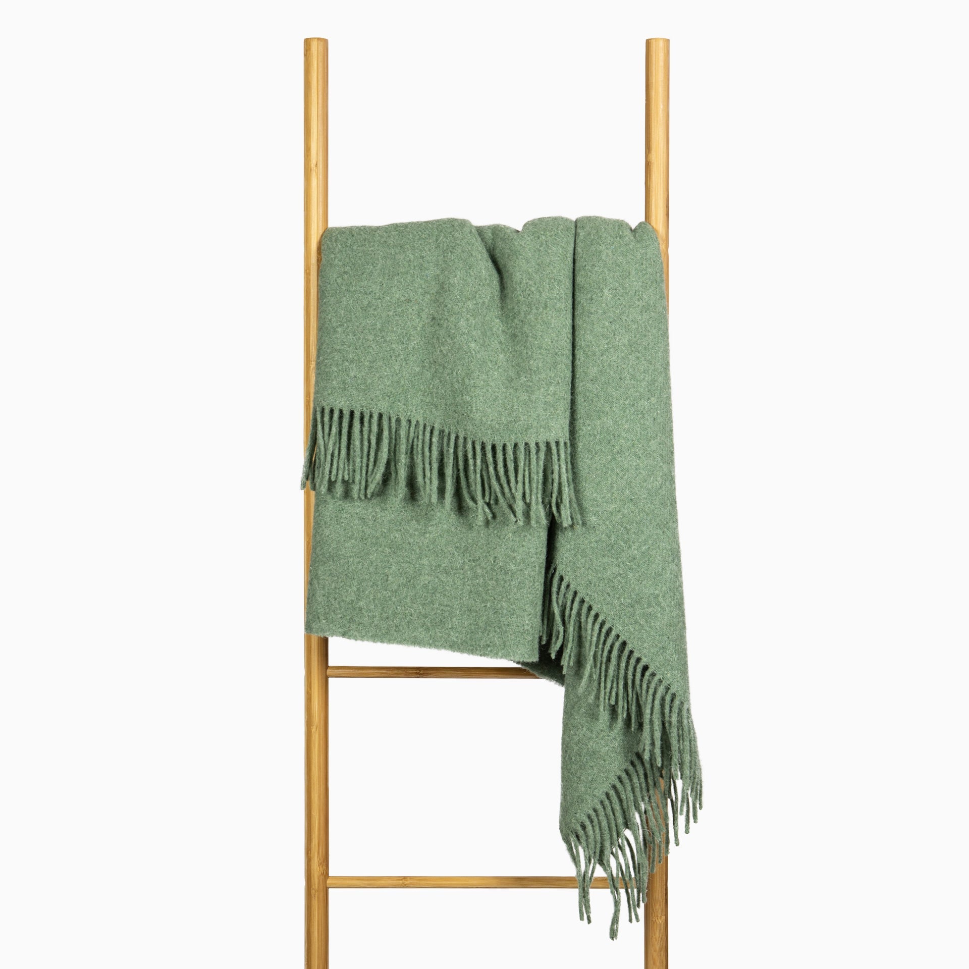 Sage green wool throw draped over ladder rack with long fringes