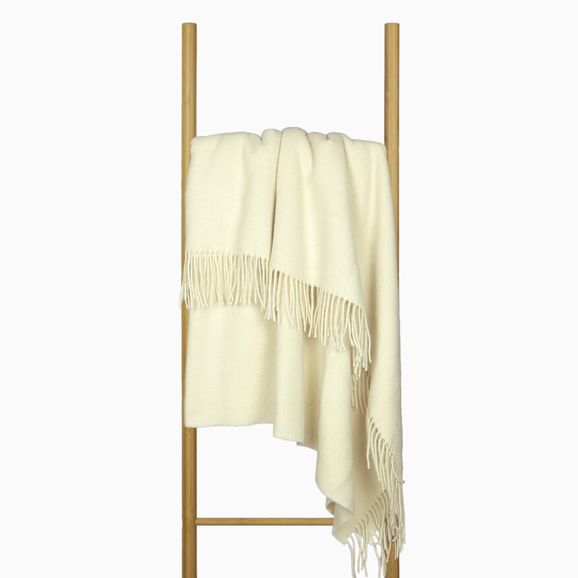 Ivory merino wool blend throw blanket draped with fringed border on stand