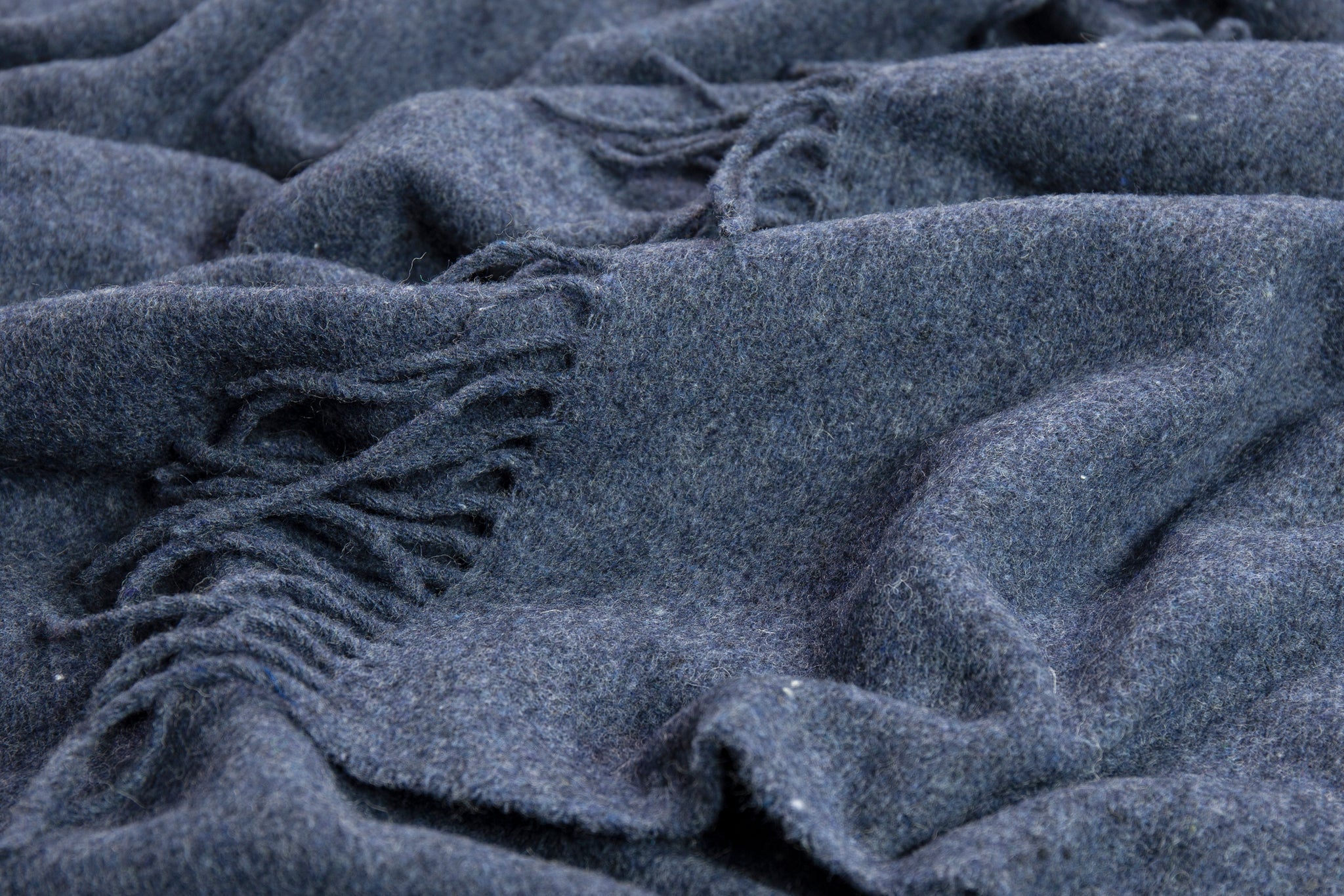 Close-up of navy wool-blend throw fabric with woven texture and fringes.