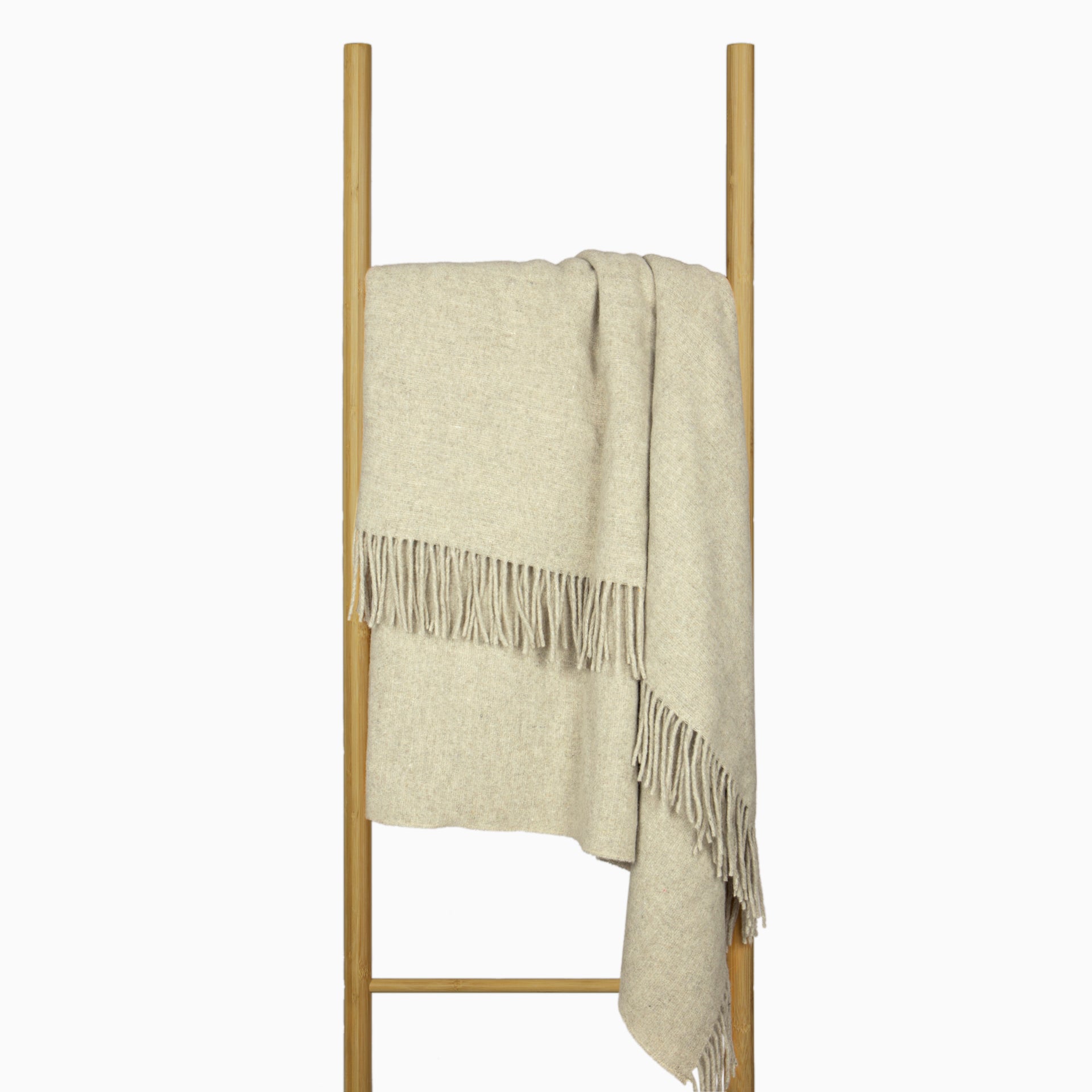 Stone merino wool blend throw blanket draped over stand, fringed border