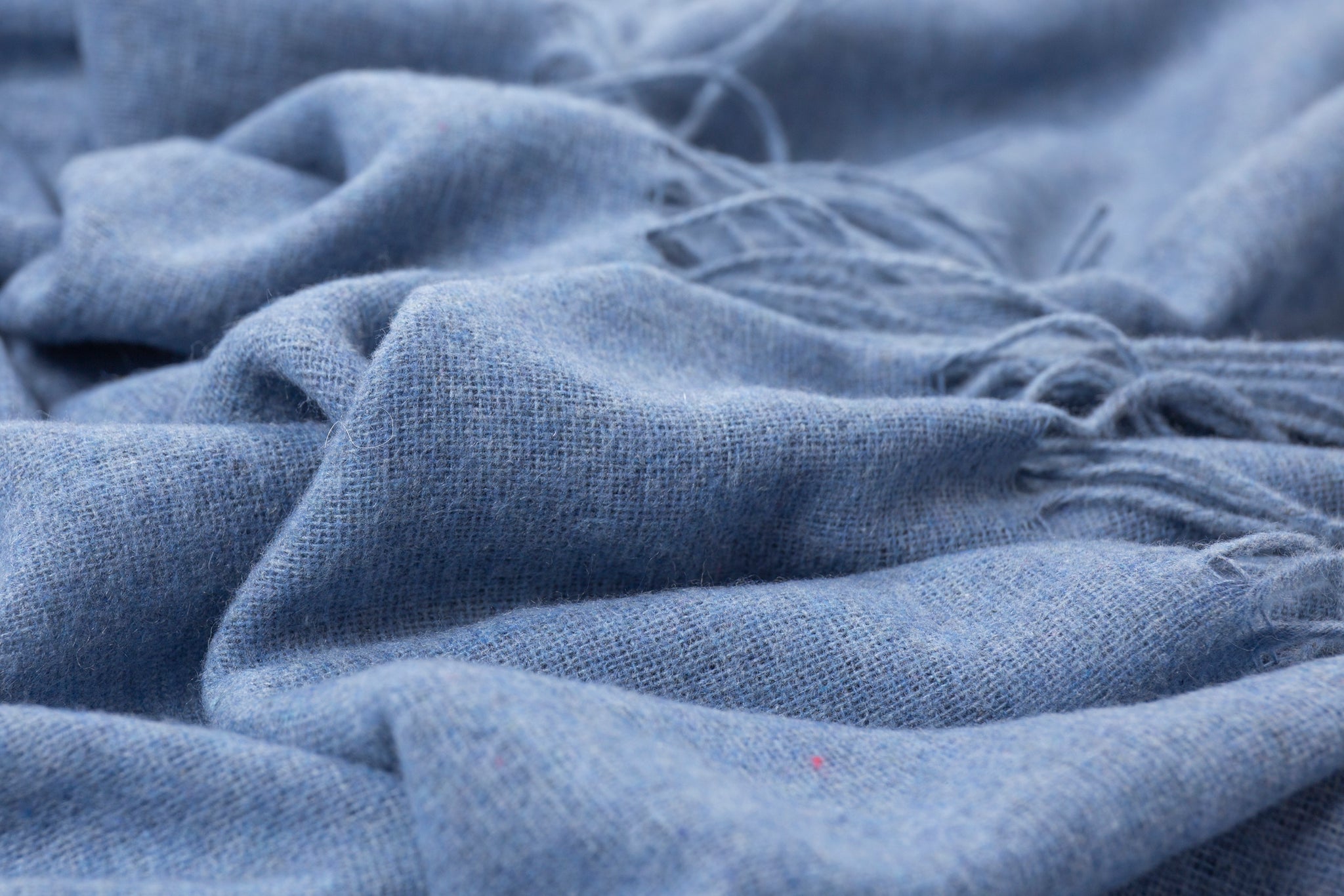 Blue throw blanket fabric close-up with soft woven texture and fringe threads