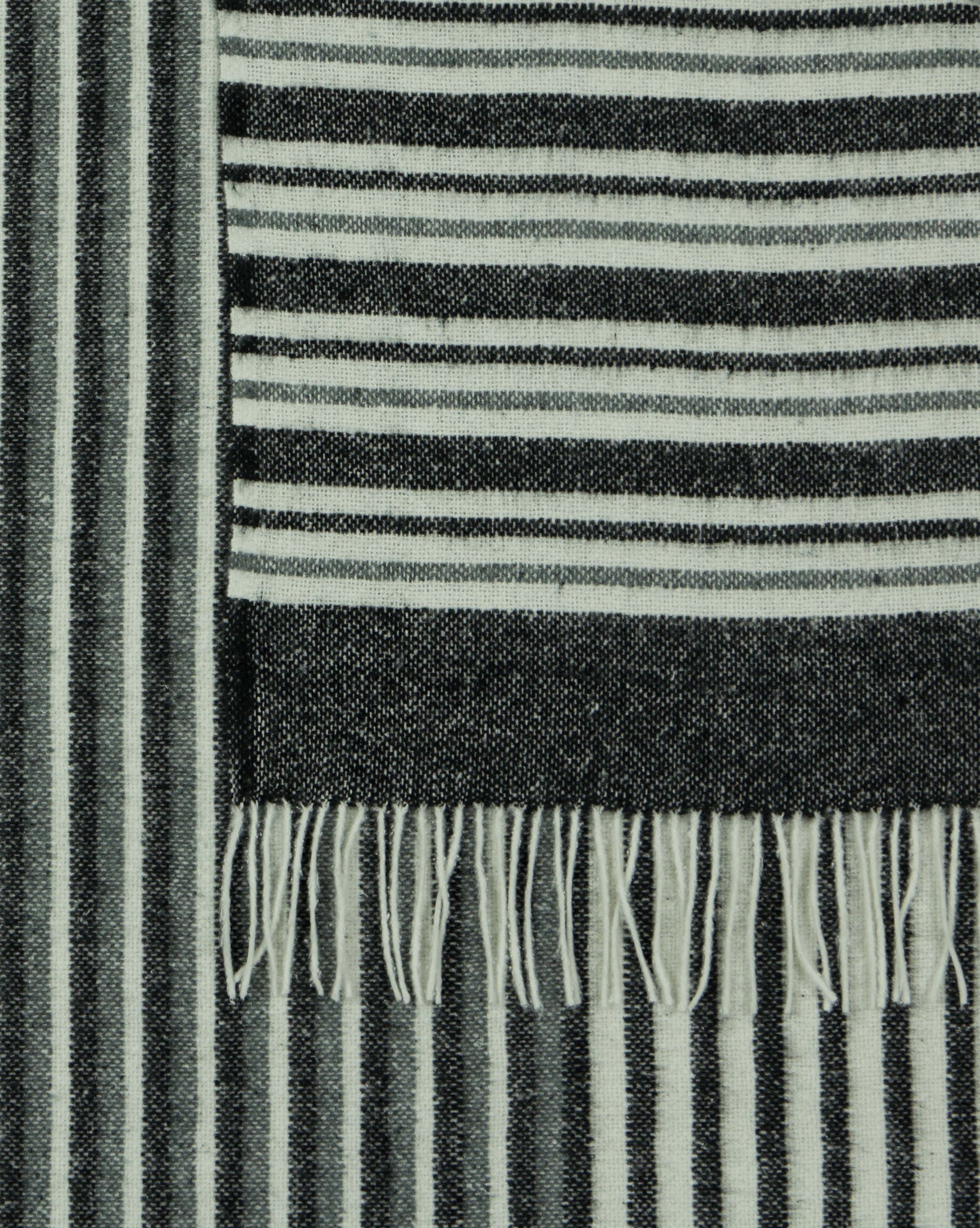 Monochrome striped throw blanket close-up with fringed hem and textured weave.