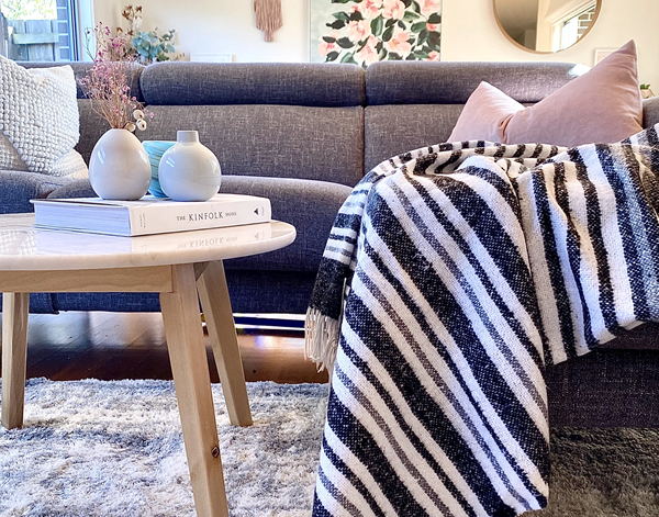 Monochrome striped throw blanket draped on sofa, with long fringed edge.
