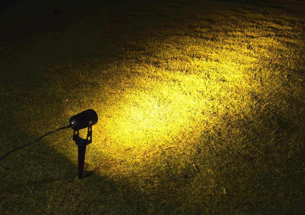 Black solar LED spotlight with spike stake casting warm light on grass