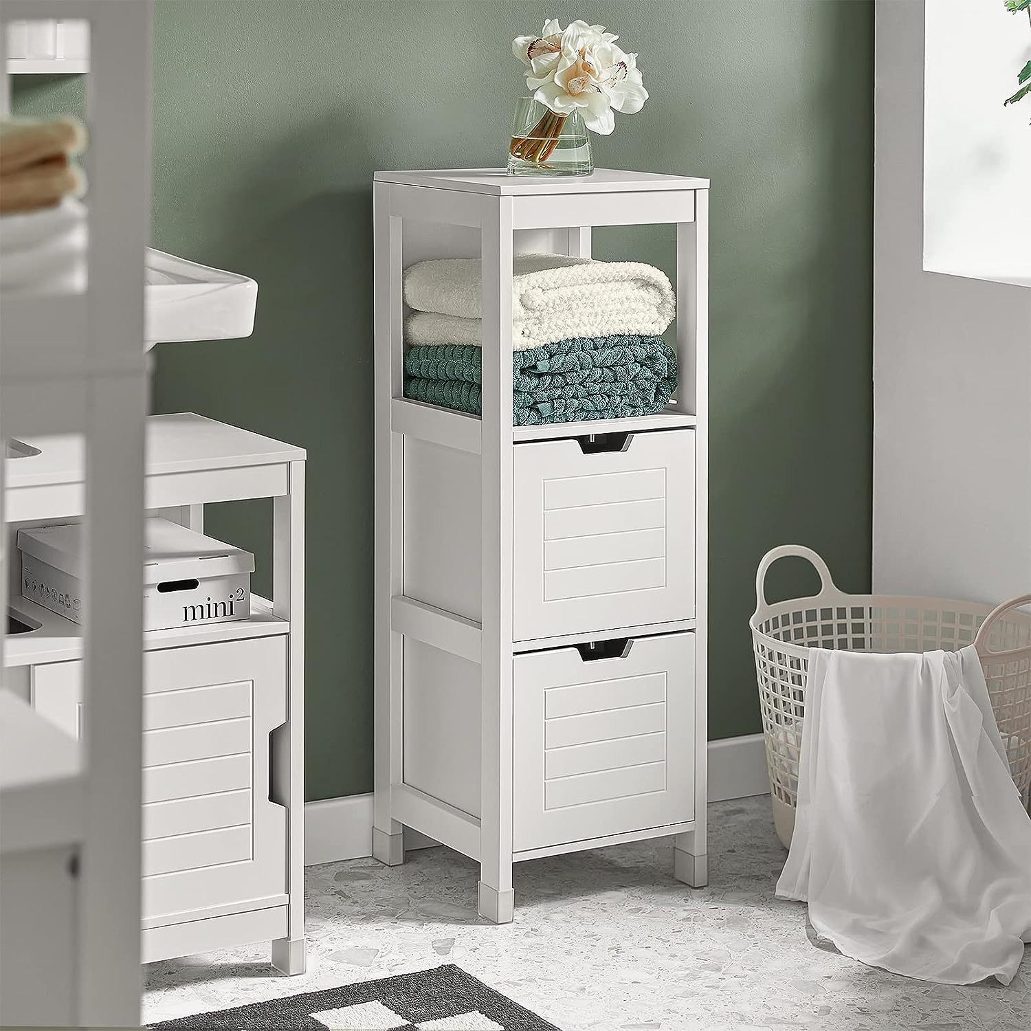 White freestanding cabinet with open shelves and two drawers, holding folded towels