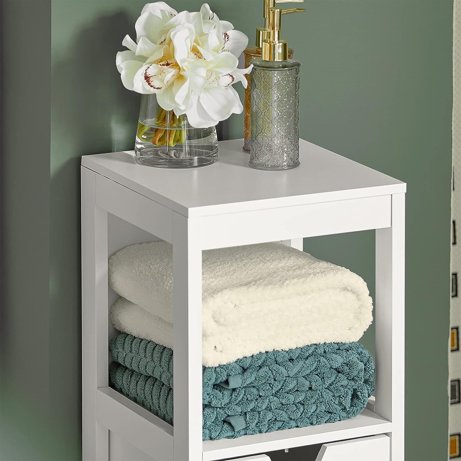 White freestanding cabinet with open shelves and two drawers, holding folded towels