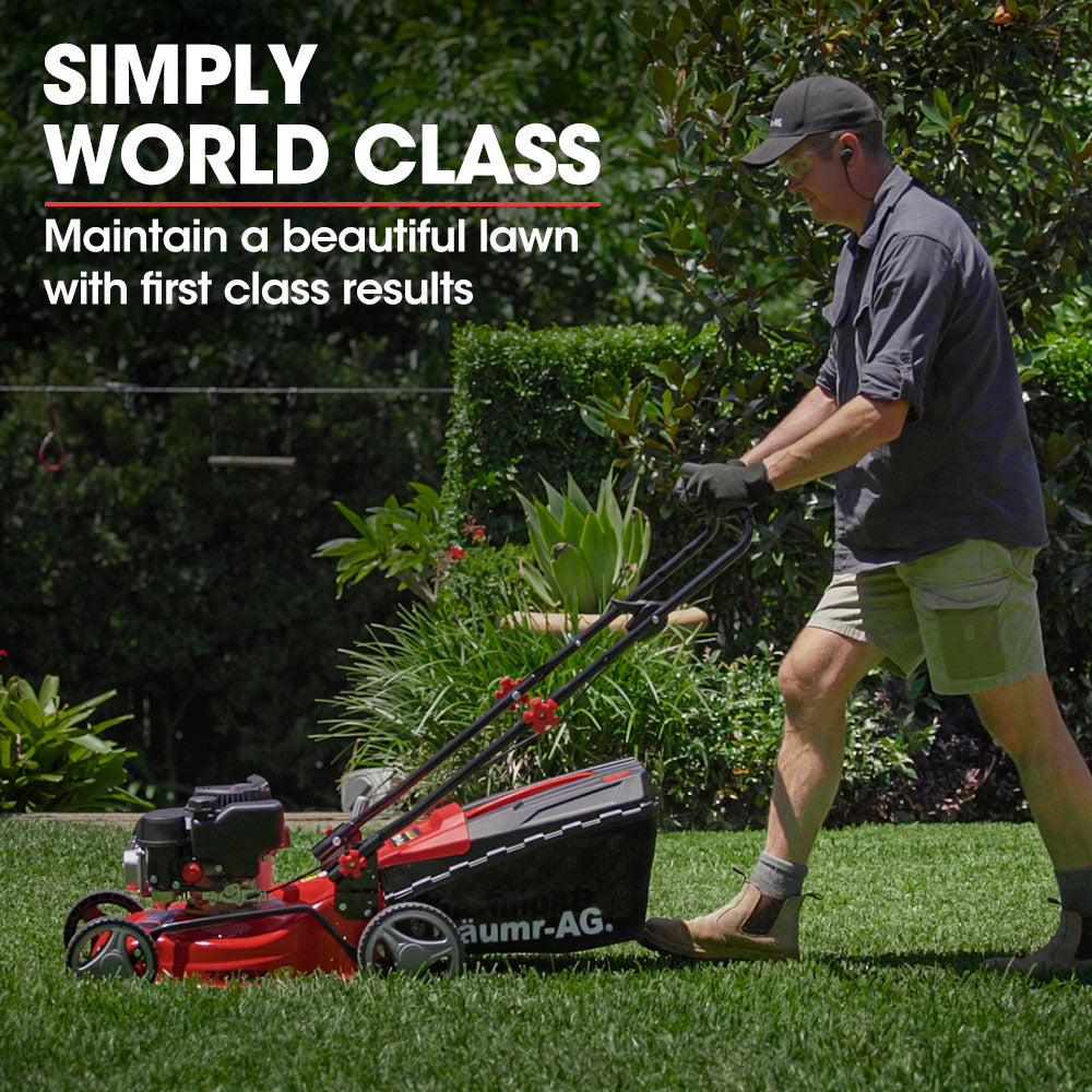 Red petrol push lawn mower being pushed across grass, showing handle and wheels