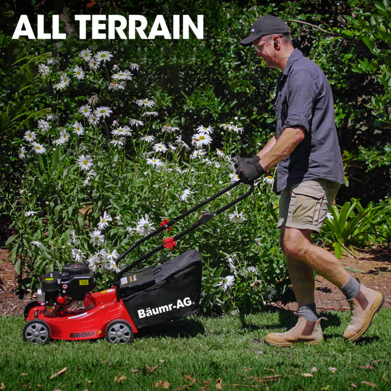Petrol push lawn mower with rear grass catcher on an uneven garden area.