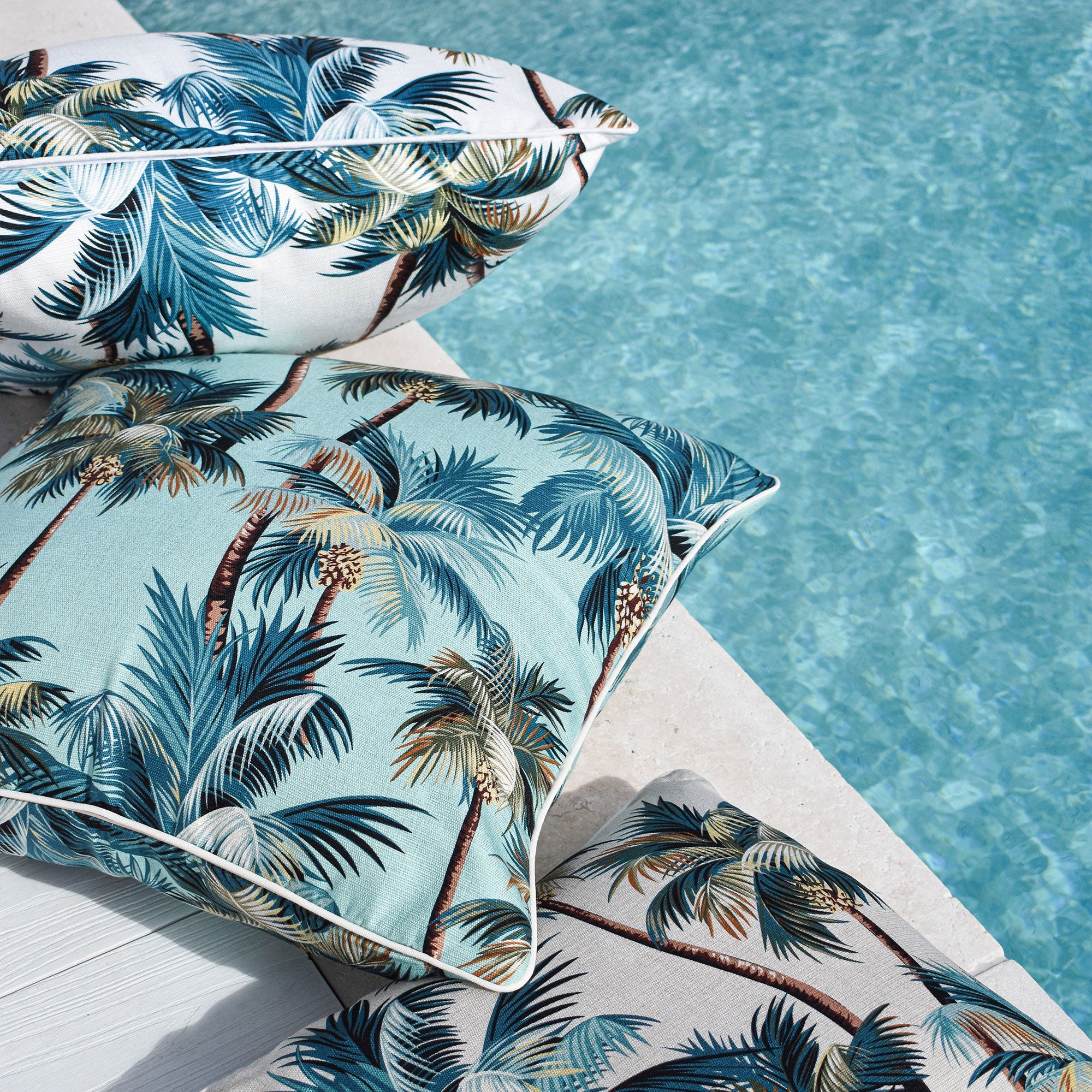 Palm tree cushion cover close-up, cream fabric with teal-blue palm leaves and piping