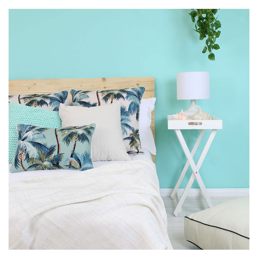Palm tree cushion cover with piping, cream fabric and teal-blue palm leaves on bed