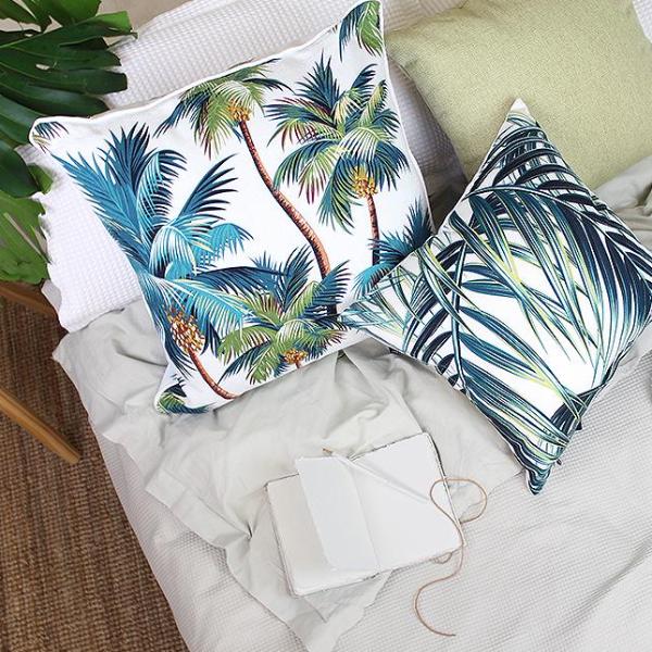 White cushion cover with teal palm tree print beside a striped cushion on bedding