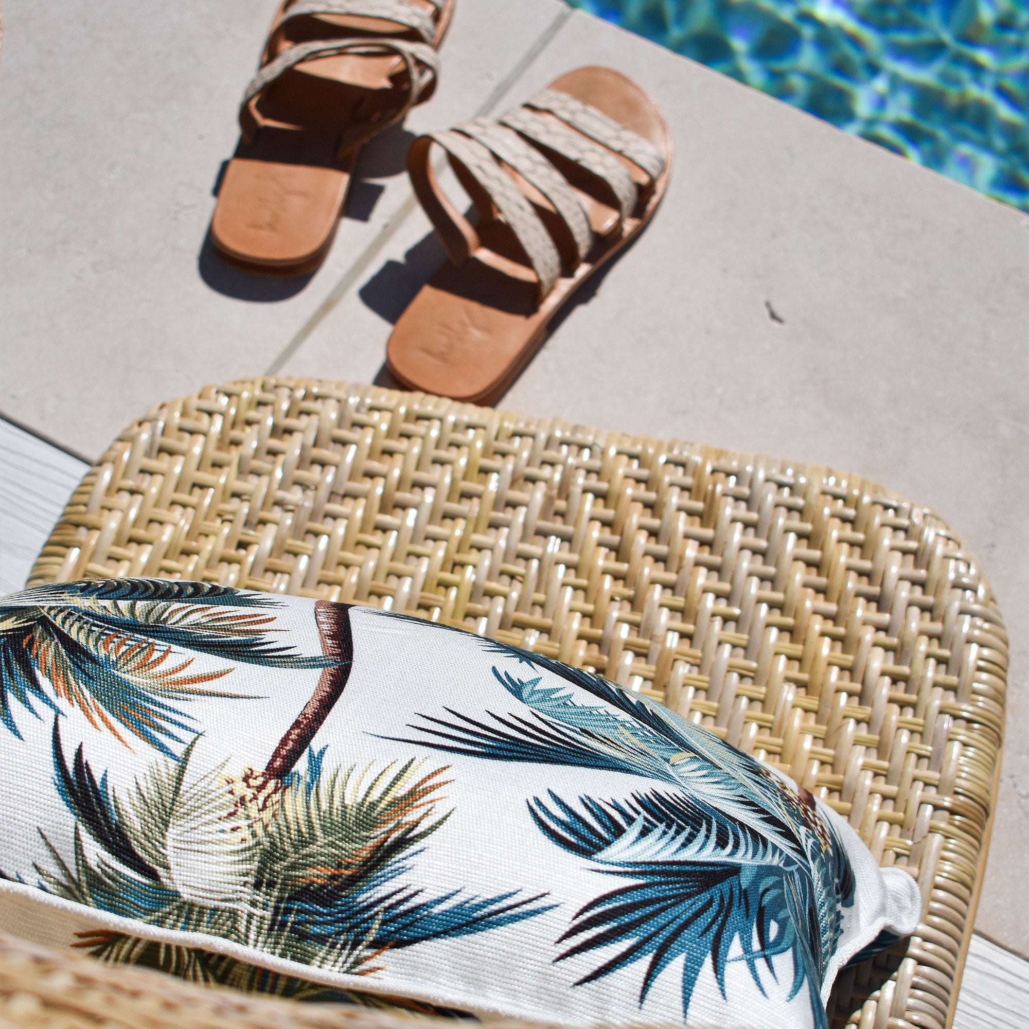 White cushion cover with teal palm leaves, placed on a woven rattan seat