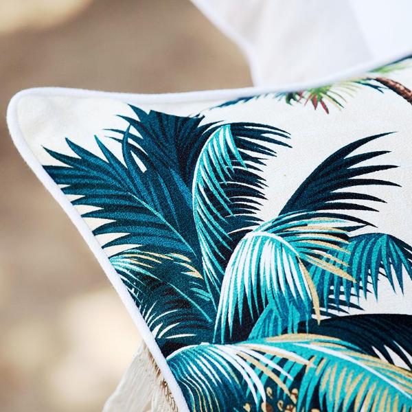 Corner of a white cushion cover with bold teal palm leaf print and piping trim
