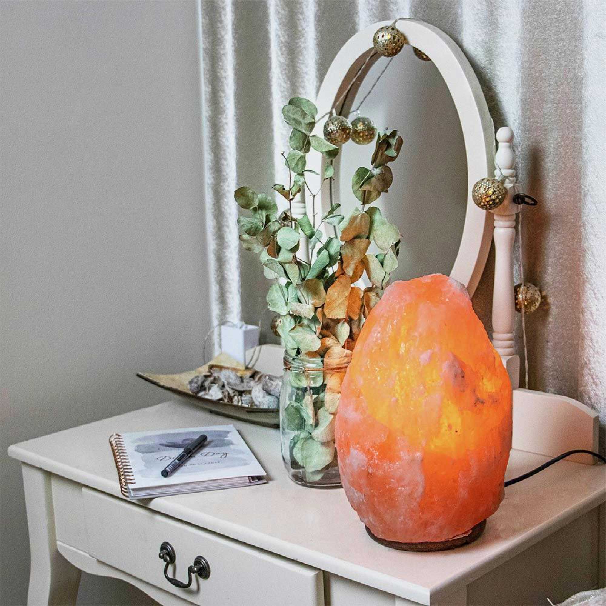 Pink Himalayan salt lamp glowing on a table next to a vase with leaves
